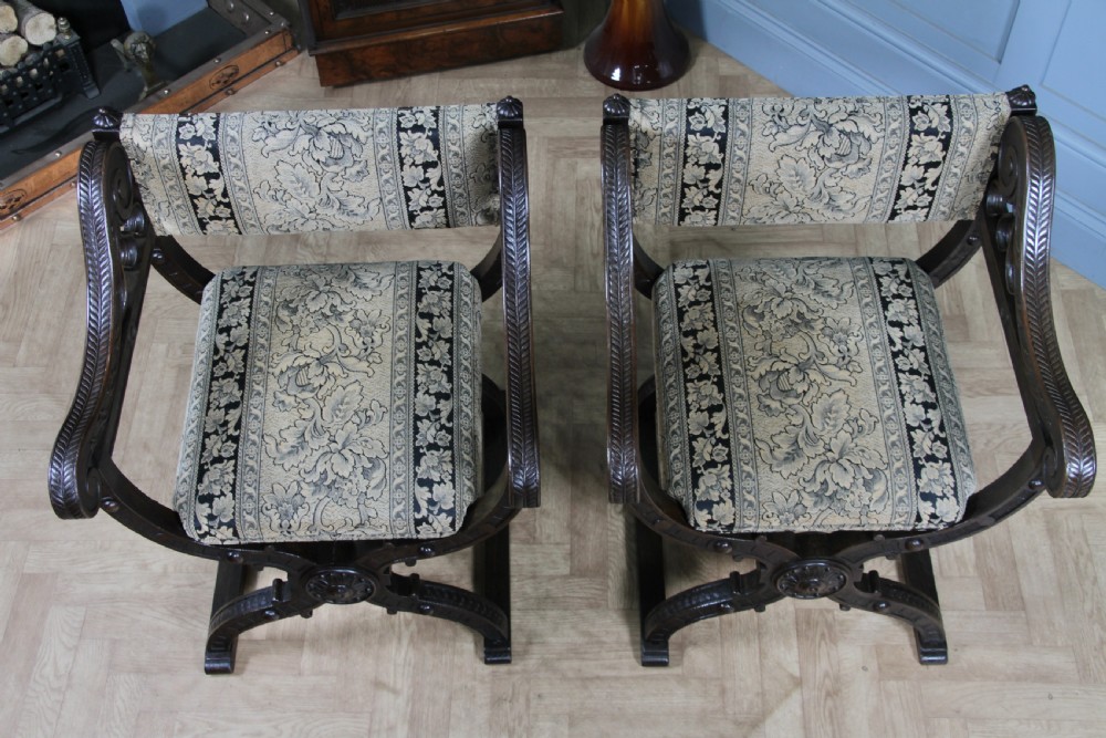 A pair of carved dark oak x-frame curule armchairs featuring patterned floral upholstery and central carved rosette bosses on the legs. View XXII