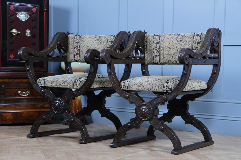 A pair of carved dark oak x-frame curule armchairs featuring patterned floral upholstery and central carved rosette bosses on the legs. View XXIV
