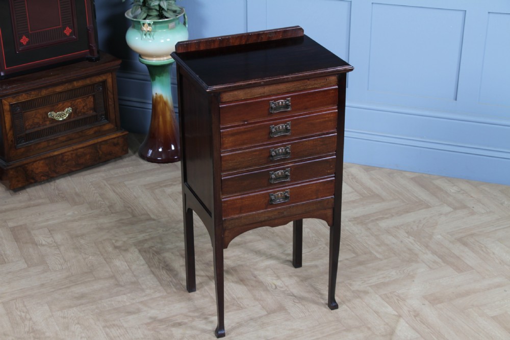 An Edwardian mahogany sheet music cabinet featuring five drop-front drawers fitted with Art Nouveau brass handles set on slender square legs. View V