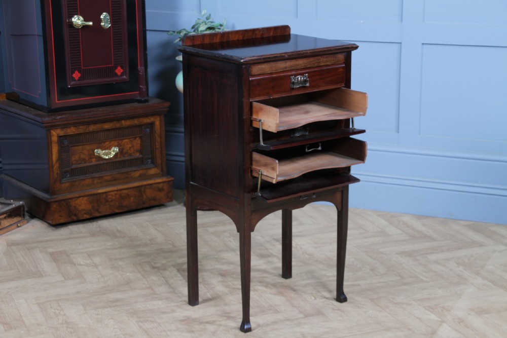An Edwardian mahogany sheet music cabinet featuring five drop-front drawers fitted with Art Nouveau brass handles set on slender square legs. View VI