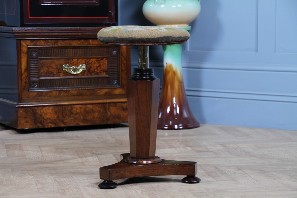 An early Victorian rosewood revolving piano stool featuring a circular floral needlepoint seat, a faceted central column, and a solid triform base with turned feet. View II