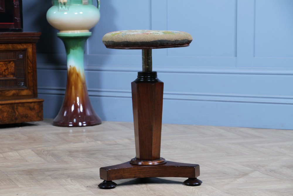An early Victorian rosewood revolving piano stool featuring a circular floral needlepoint seat, a faceted central column, and a solid triform base with turned feet. View III