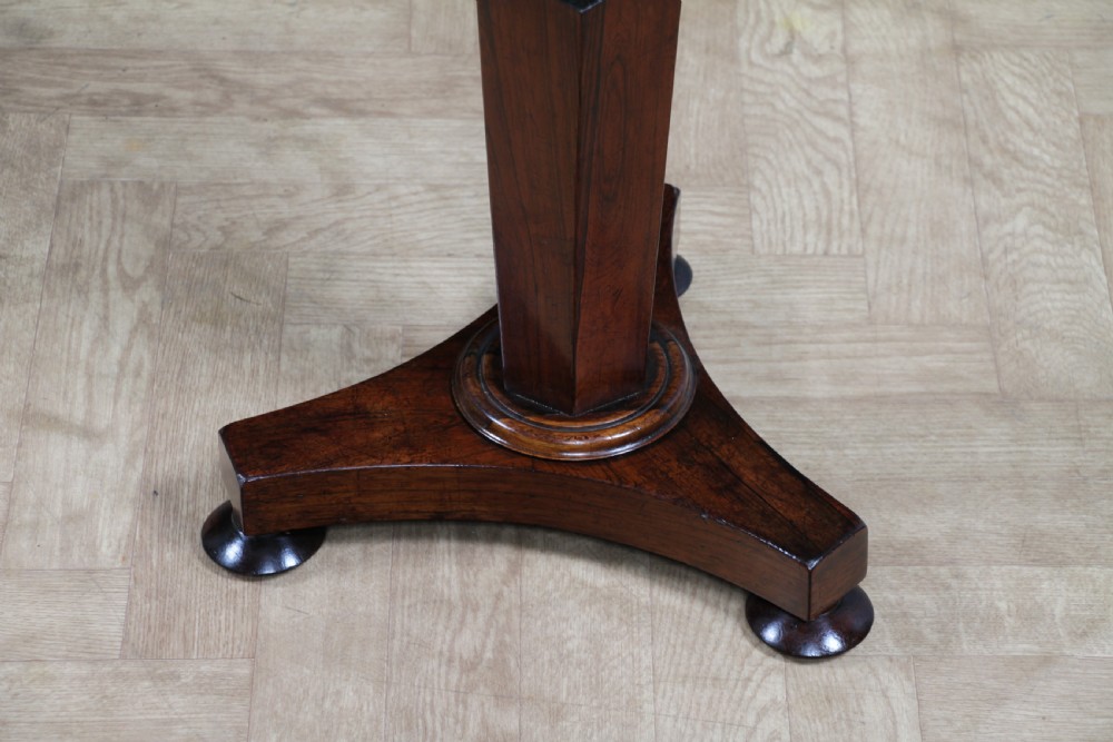An early Victorian rosewood revolving piano stool featuring a circular floral needlepoint seat, a faceted central column, and a solid triform base with turned feet. View VI