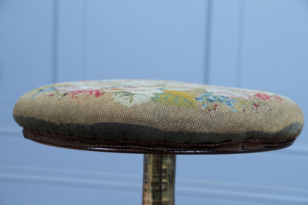 An early Victorian rosewood revolving piano stool featuring a circular floral needlepoint seat, a faceted central column, and a solid triform base with turned feet. View VIII