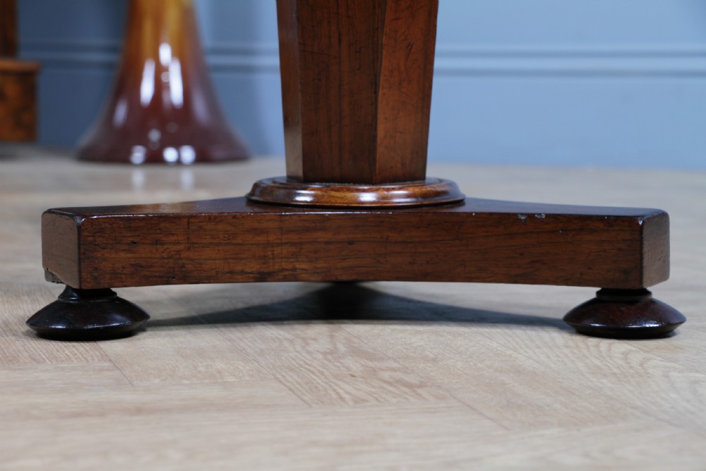 An early Victorian rosewood revolving piano stool featuring a circular floral needlepoint seat, a faceted central column, and a solid triform base with turned feet. View X
