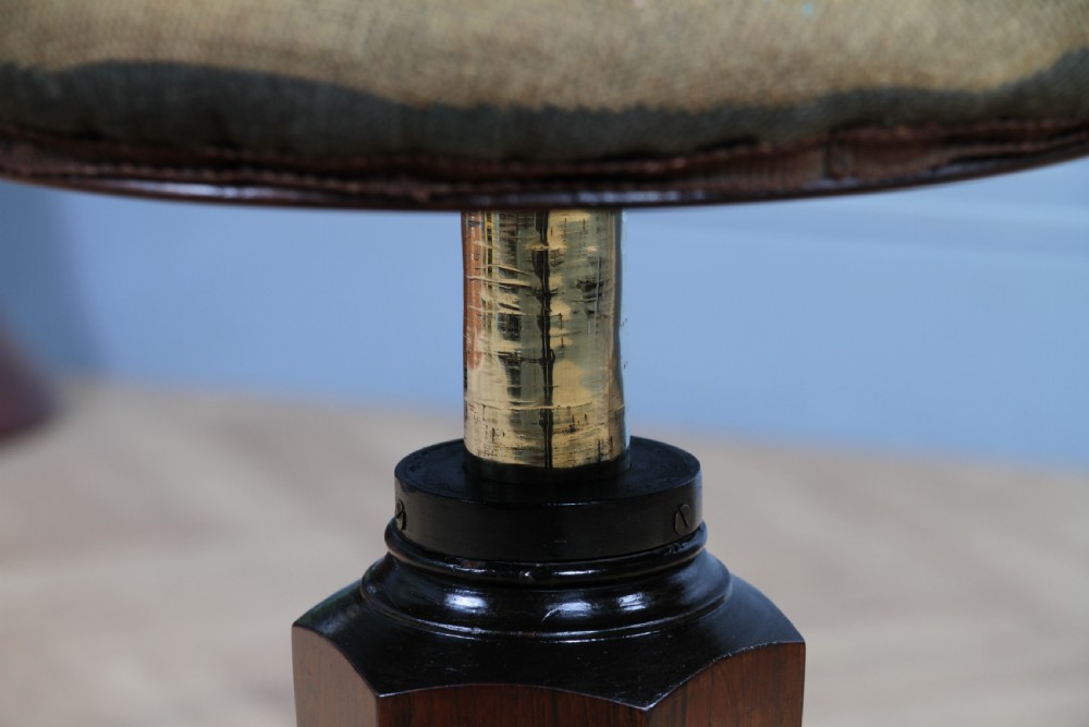 An early Victorian rosewood revolving piano stool featuring a circular floral needlepoint seat, a faceted central column, and a solid triform base with turned feet. View XI