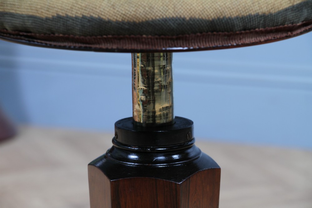 An early Victorian rosewood revolving piano stool featuring a circular floral needlepoint seat, a faceted central column, and a solid triform base with turned feet. View XII