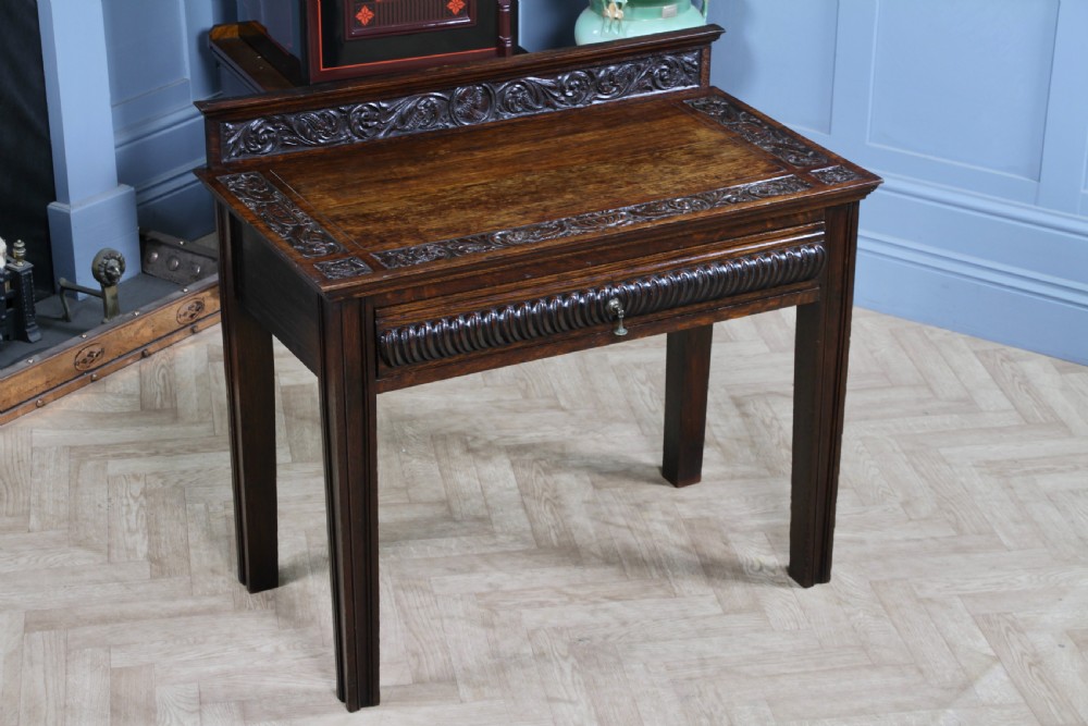 A dark carved oak side desk featuring a carved low gallery back, border-carved top surface, a single fluted drawer, and reeded legs. View II
