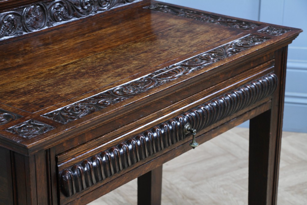 A dark carved oak side desk featuring a carved low gallery back, border-carved top surface, a single fluted drawer, and reeded legs. View III