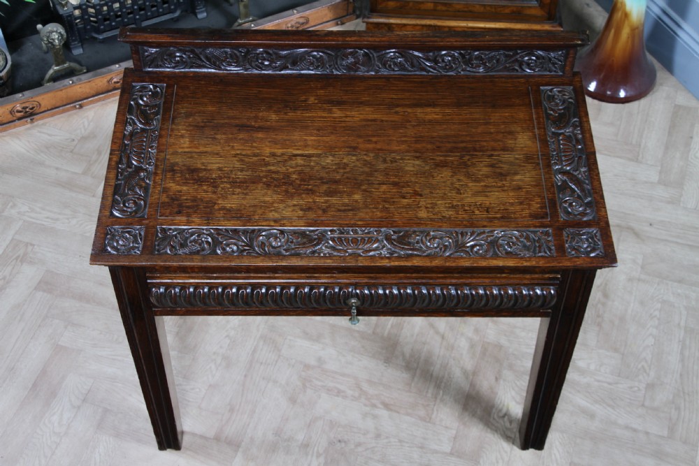 A dark carved oak side desk featuring a carved low gallery back, border-carved top surface, a single fluted drawer, and reeded legs. View IV