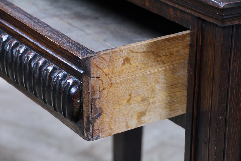 A dark carved oak side desk featuring a carved low gallery back, border-carved top surface, a single fluted drawer, and reeded legs. View V