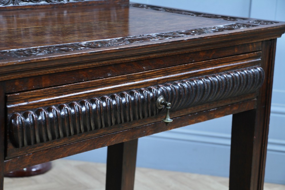 A dark carved oak side desk featuring a carved low gallery back, border-carved top surface, a single fluted drawer, and reeded legs. View VI