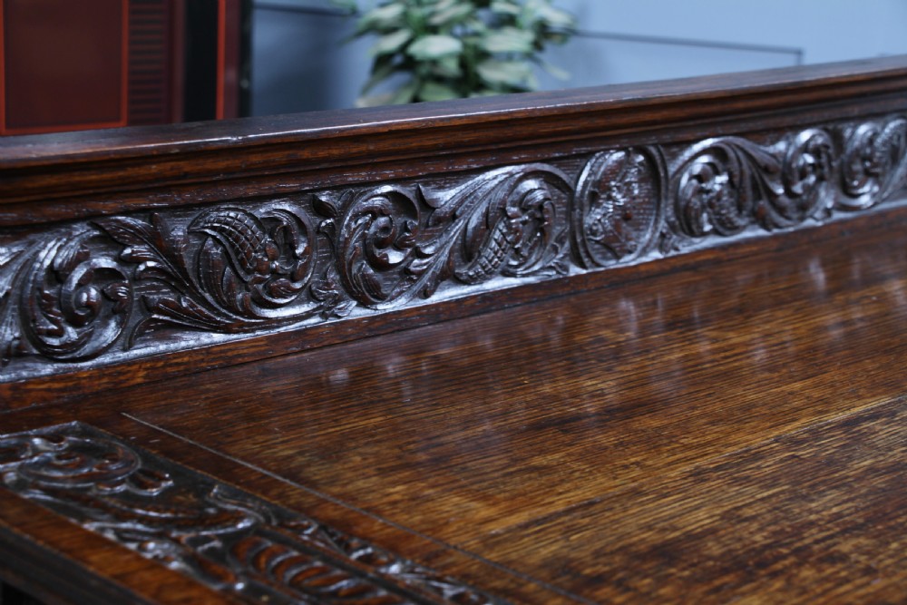A dark carved oak side desk featuring a carved low gallery back, border-carved top surface, a single fluted drawer, and reeded legs. View VIII