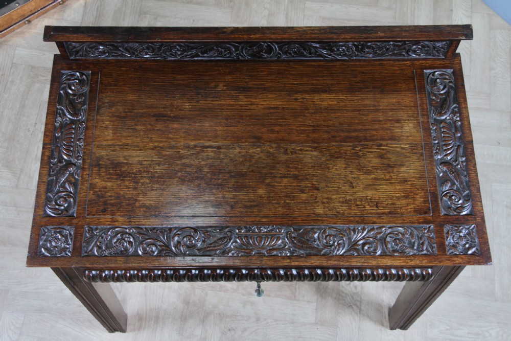 A dark carved oak side desk featuring a carved low gallery back, border-carved top surface, a single fluted drawer, and reeded legs. View XII