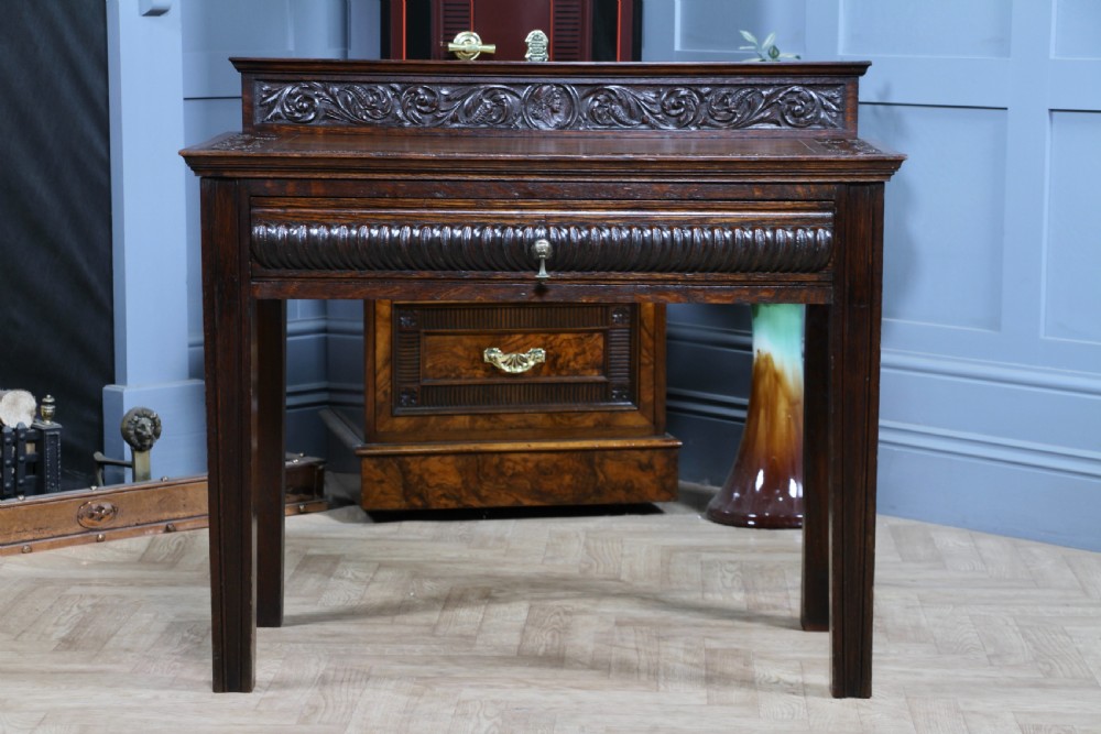 A dark carved oak side desk featuring a carved low gallery back, border-carved top surface, a single fluted drawer, and reeded legs. View XIII