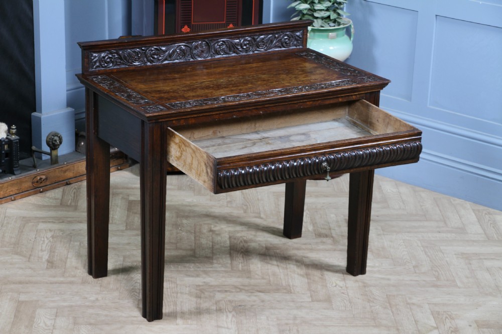 A dark carved oak side desk featuring a carved low gallery back, border-carved top surface, a single fluted drawer, and reeded legs. View XIV