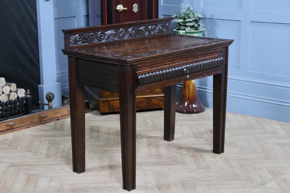 A dark carved oak side desk featuring a carved low gallery back, border-carved top surface, a single fluted drawer, and reeded legs. View XV