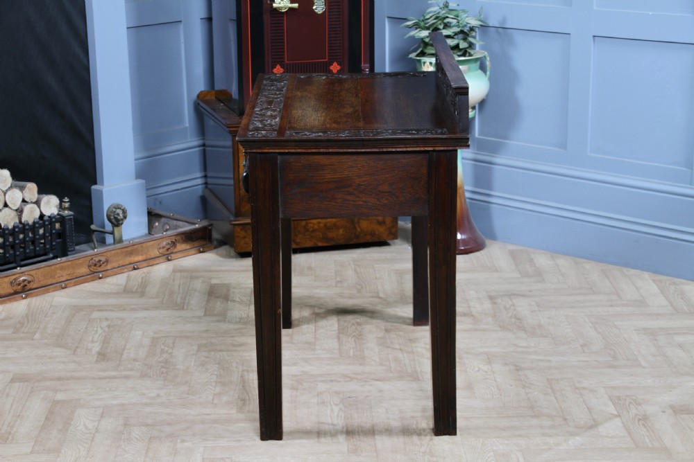 A dark carved oak side desk featuring a carved low gallery back, border-carved top surface, a single fluted drawer, and reeded legs. View XVI