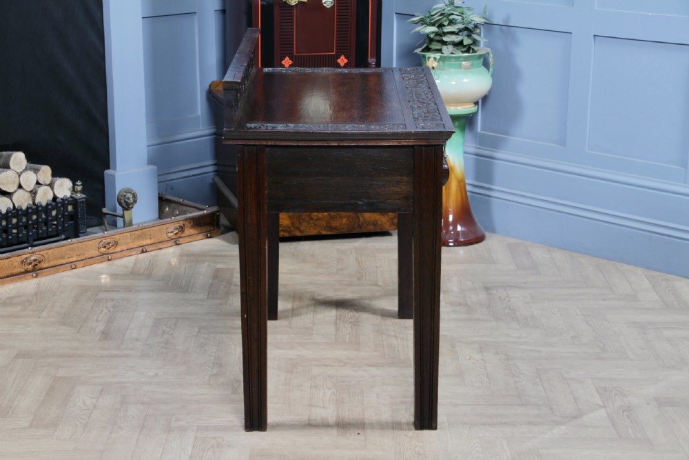 A dark carved oak side desk featuring a carved low gallery back, border-carved top surface, a single fluted drawer, and reeded legs. View XVII