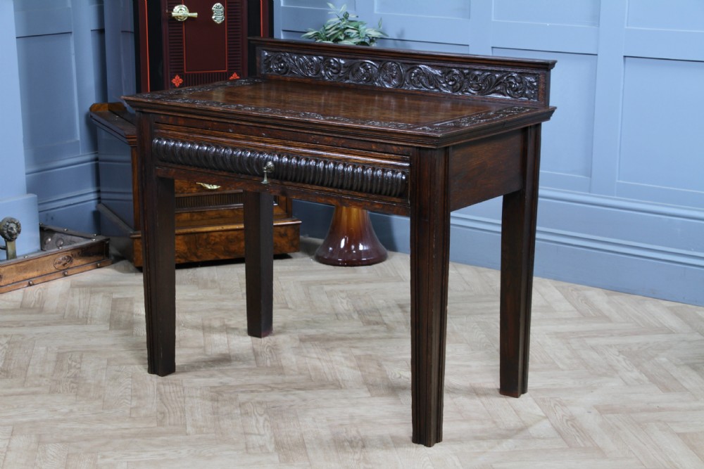A dark carved oak side desk featuring a carved low gallery back, border-carved top surface, a single fluted drawer, and reeded legs. View XVIII