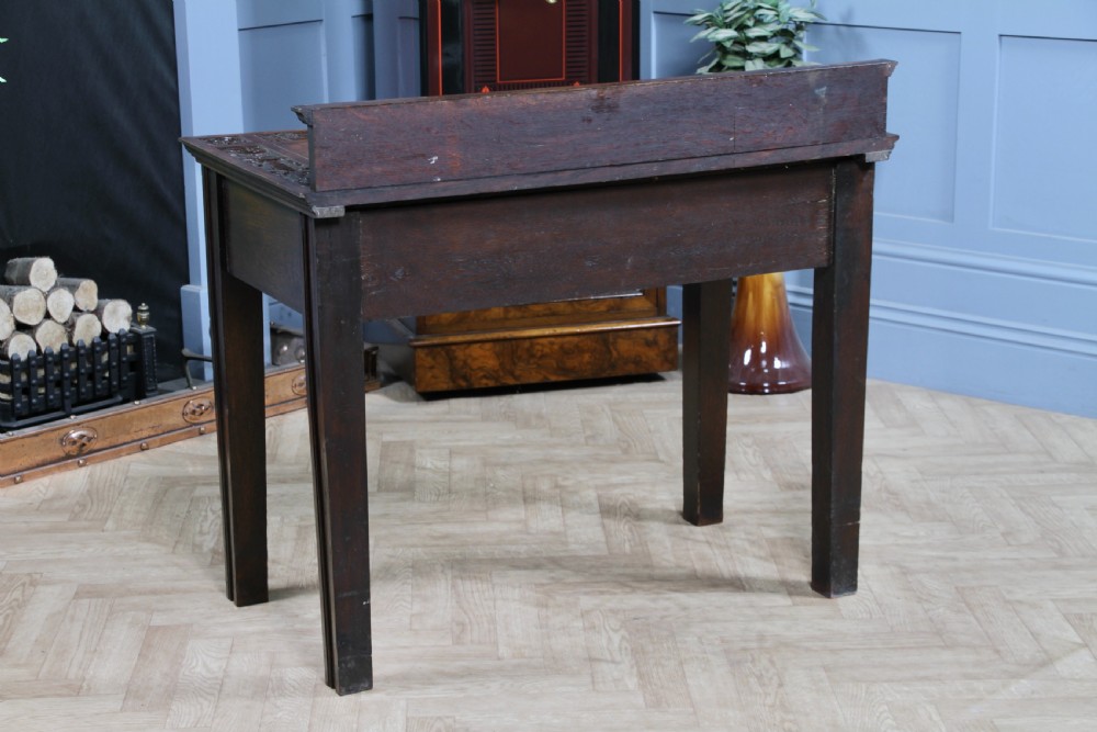 A dark carved oak side desk featuring a carved low gallery back, border-carved top surface, a single fluted drawer, and reeded legs. View XIX