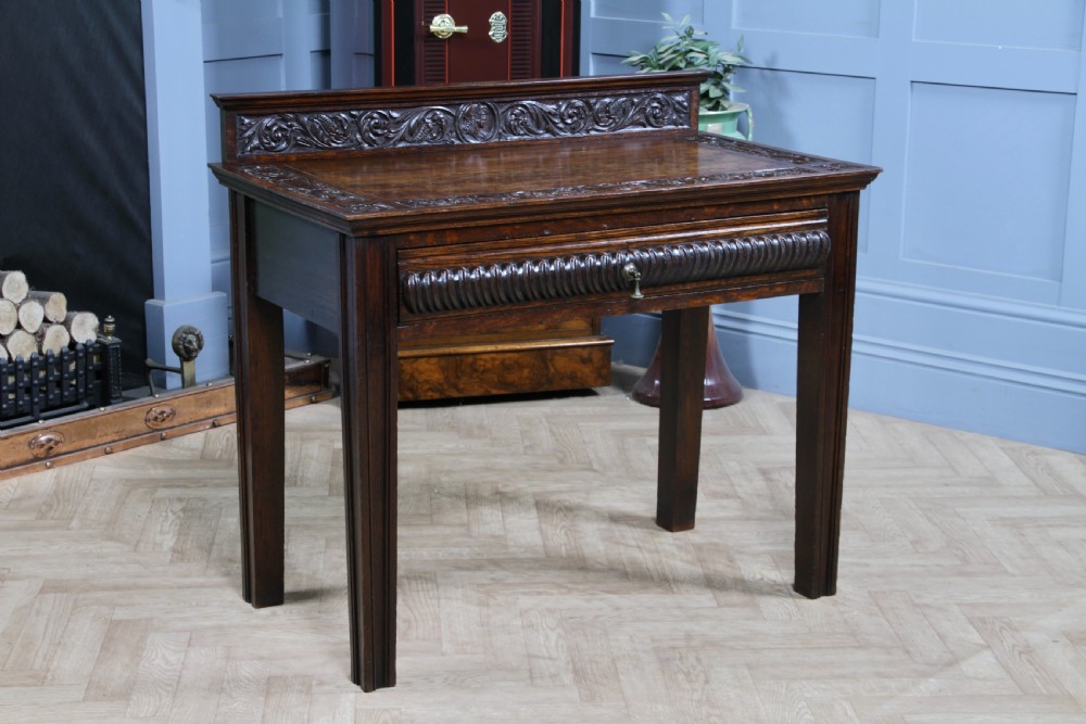 A dark carved oak side desk featuring a carved low gallery back, border-carved top surface, a single fluted drawer, and reeded legs. View XX