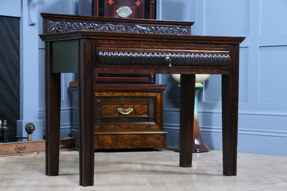 A dark carved oak side desk featuring a carved low gallery back, border-carved top surface, a single fluted drawer, and reeded legs. View XXI