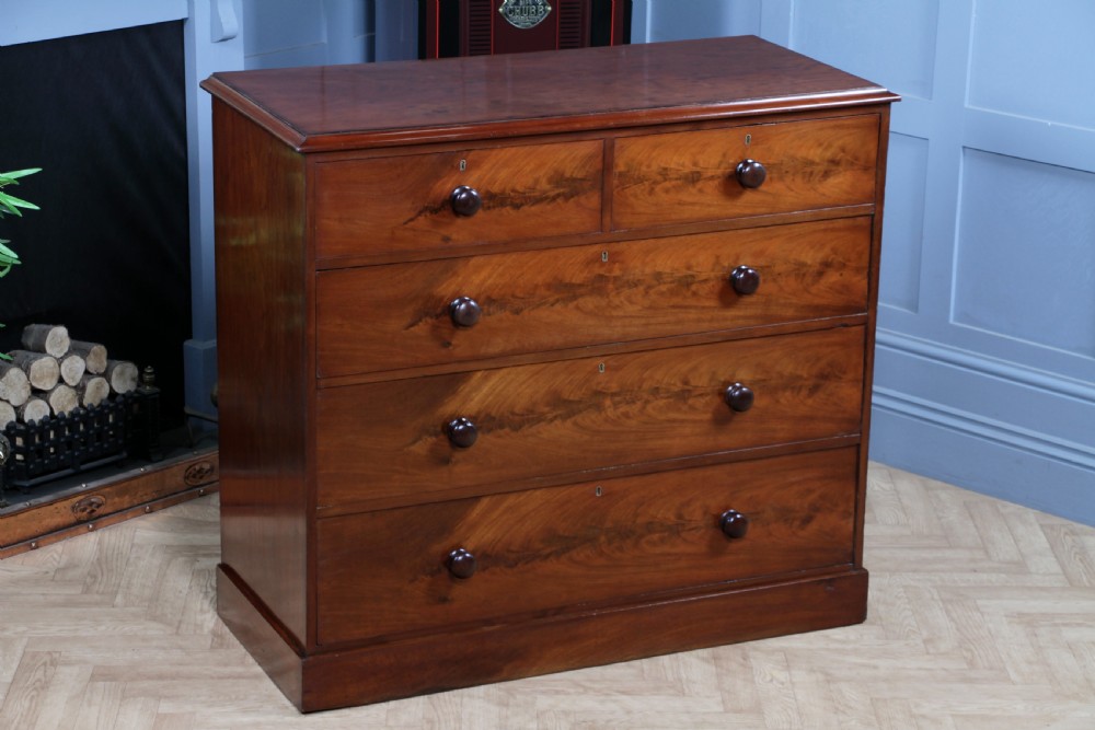 An antique Victorian flame mahogany chest of drawers featuring two short over three long drawers with turned wooden handles on a solid plinth base.