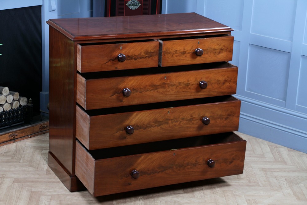 An antique Victorian flame mahogany chest of drawers featuring two short over three long drawers with turned wooden handles on a solid plinth base. View II