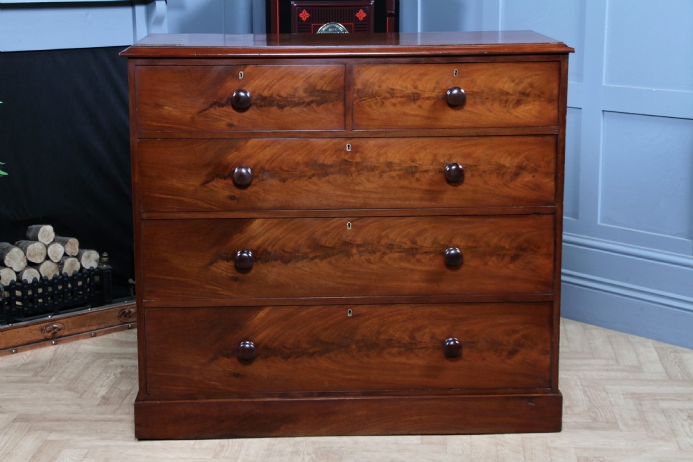 An antique Victorian flame mahogany chest of drawers featuring two short over three long drawers with turned wooden handles on a solid plinth base. View III