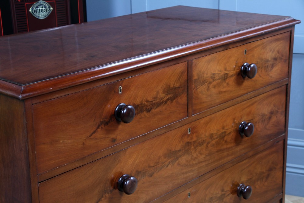 An antique Victorian flame mahogany chest of drawers featuring two short over three long drawers with turned wooden handles on a solid plinth base. View IV
