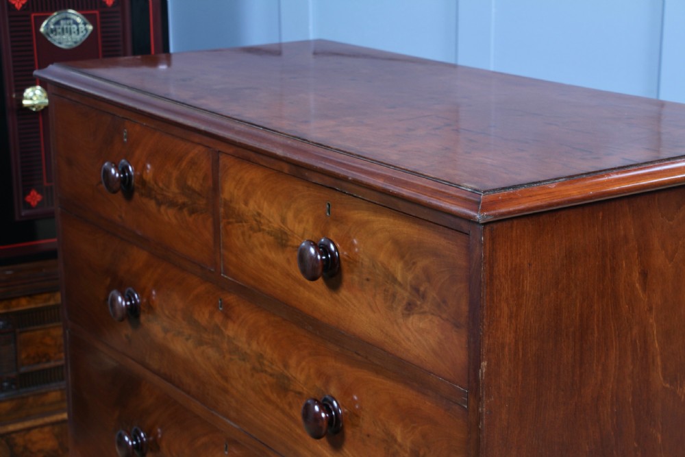 An antique Victorian flame mahogany chest of drawers featuring two short over three long drawers with turned wooden handles on a solid plinth base. View V