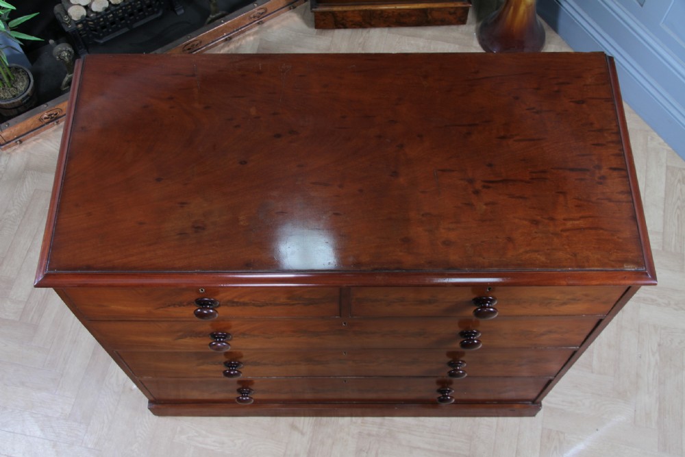 An antique Victorian flame mahogany chest of drawers featuring two short over three long drawers with turned wooden handles on a solid plinth base. View VI
