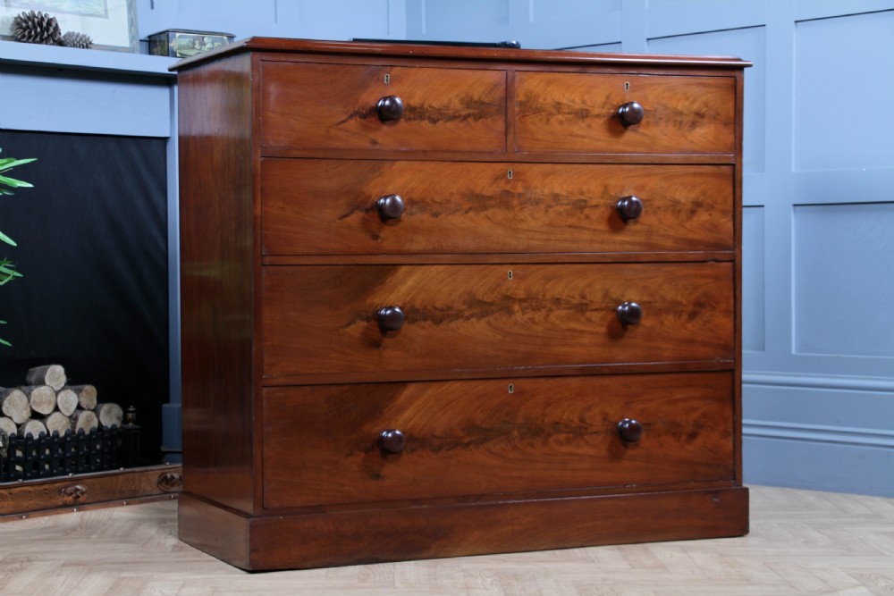 An antique Victorian flame mahogany chest of drawers featuring two short over three long drawers with turned wooden handles on a solid plinth base. View VIII