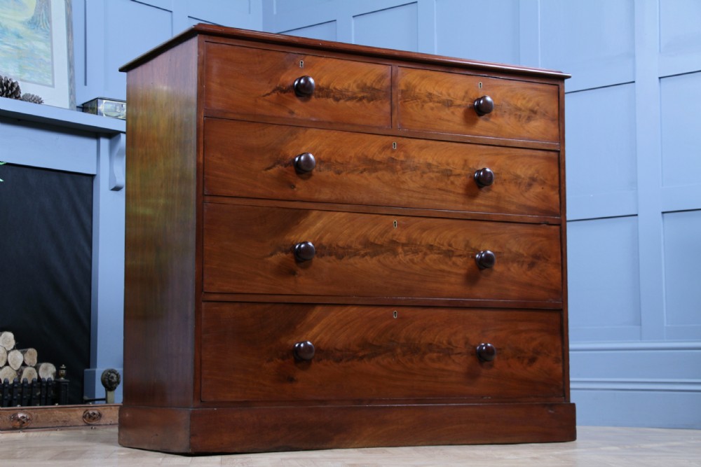 An antique Victorian flame mahogany chest of drawers featuring two short over three long drawers with turned wooden handles on a solid plinth base. View IX