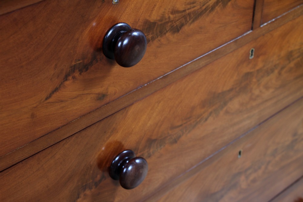 An antique Victorian flame mahogany chest of drawers featuring two short over three long drawers with turned wooden handles on a solid plinth base. View X