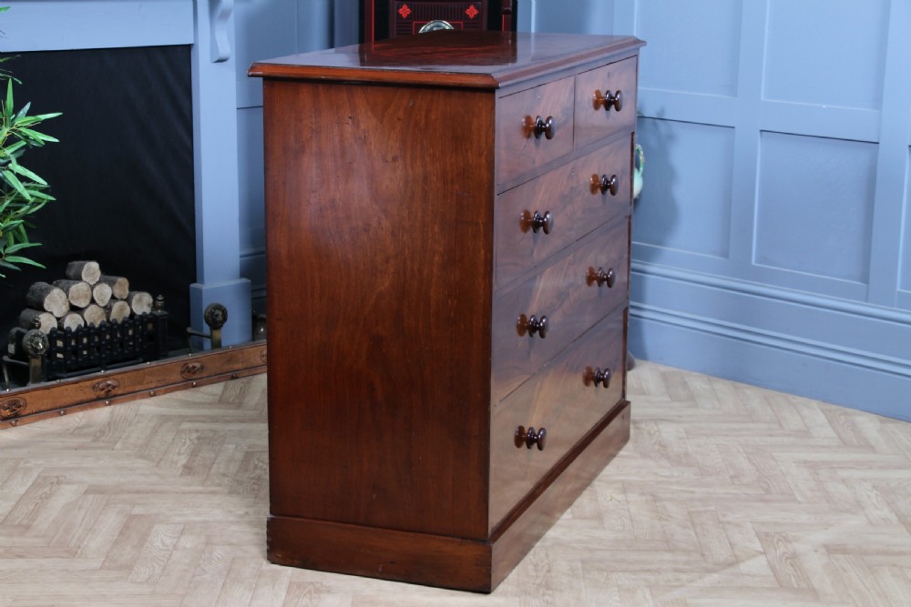 An antique Victorian flame mahogany chest of drawers featuring two short over three long drawers with turned wooden handles on a solid plinth base. View XII