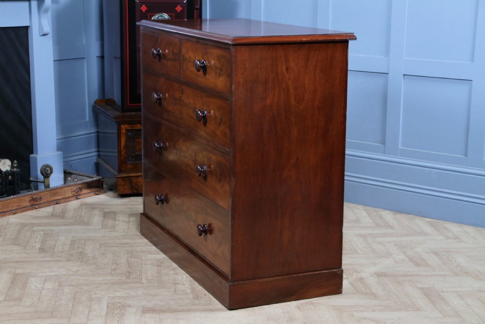 An antique Victorian flame mahogany chest of drawers featuring two short over three long drawers with turned wooden handles on a solid plinth base. View XIII