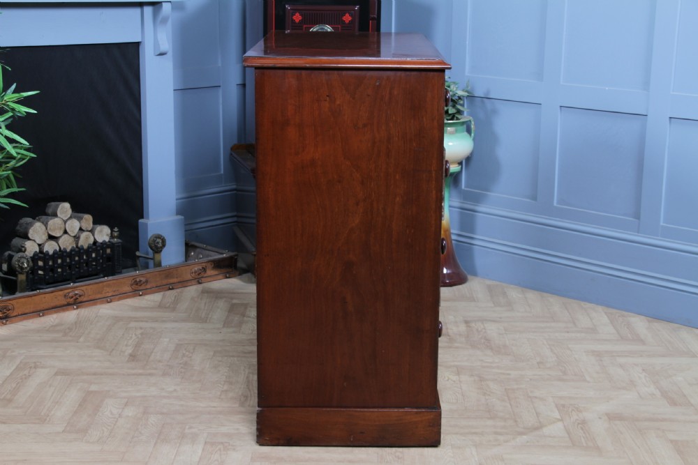 An antique Victorian flame mahogany chest of drawers featuring two short over three long drawers with turned wooden handles on a solid plinth base. View XV