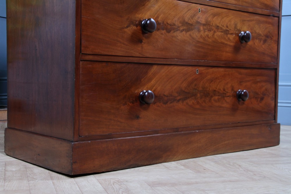An antique Victorian flame mahogany chest of drawers featuring two short over three long drawers with turned wooden handles on a solid plinth base. View XVI