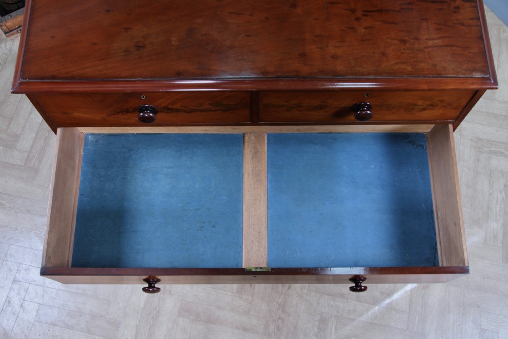 An antique Victorian flame mahogany chest of drawers featuring two short over three long drawers with turned wooden handles on a solid plinth base. View XVIII