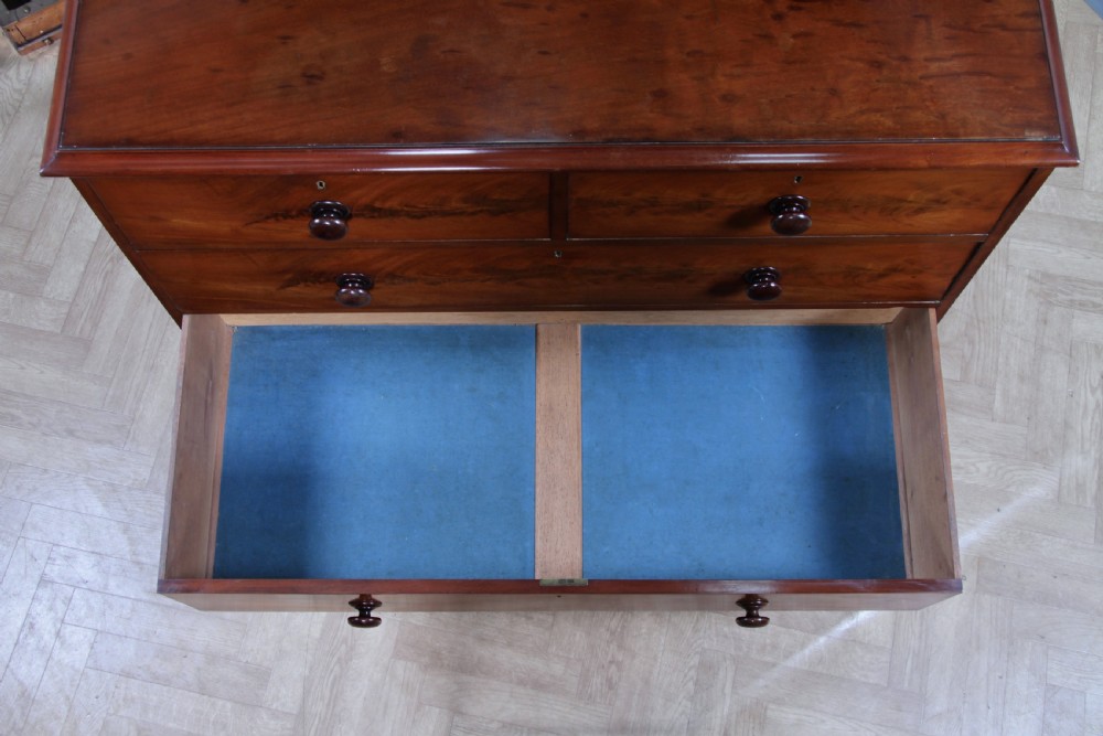 An antique Victorian flame mahogany chest of drawers featuring two short over three long drawers with turned wooden handles on a solid plinth base. View XIX