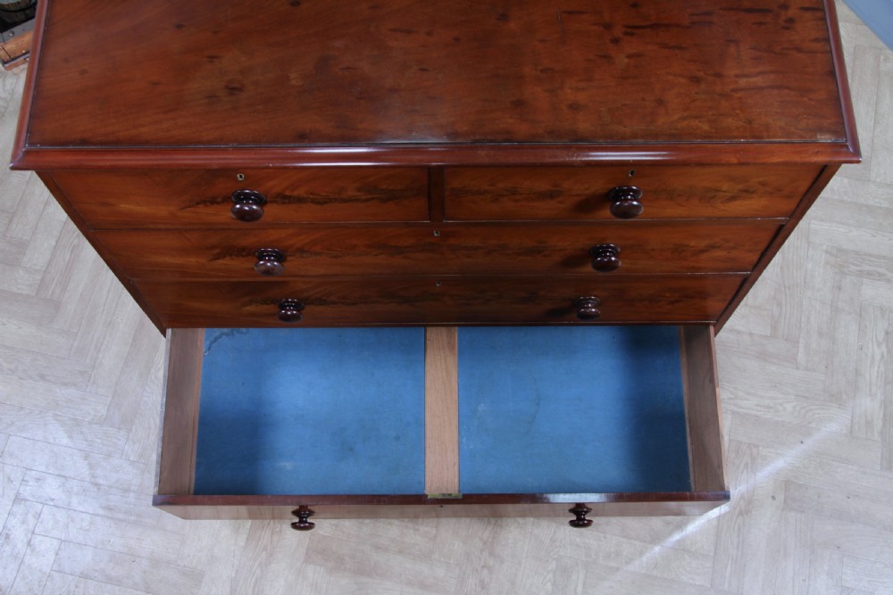 An antique Victorian flame mahogany chest of drawers featuring two short over three long drawers with turned wooden handles on a solid plinth base. View XX