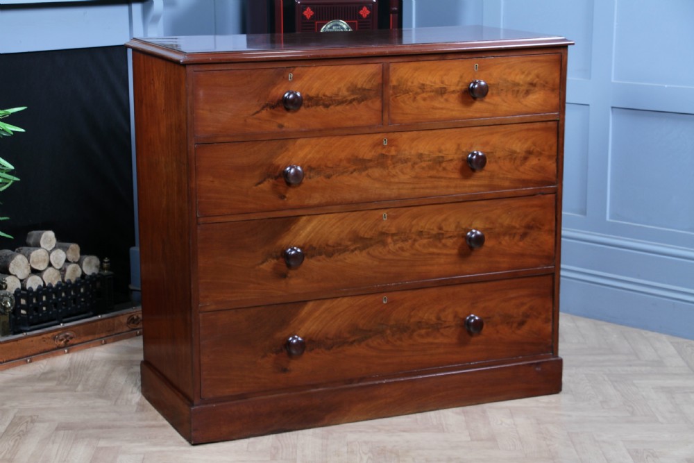 An antique Victorian flame mahogany chest of drawers featuring two short over three long drawers with turned wooden handles on a solid plinth base. View XXI