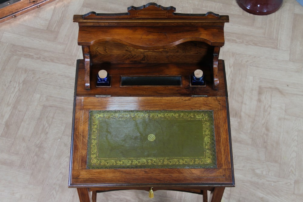 A late Victorian inlaid rosewood bonheur du jour writing desk featuring a green leather surface, raised gallery shelf, and tapered legs with brass castors. View VI