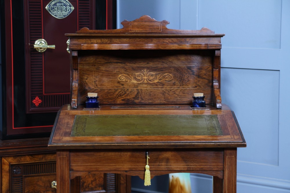 A late Victorian inlaid rosewood bonheur du jour writing desk featuring a green leather surface, raised gallery shelf, and tapered legs with brass castors. View IX