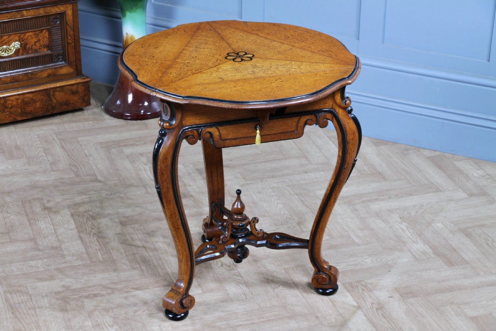 A Victorian Aesthetic Movement oak handkerchief table featuring ebonised accents, curved legs, and a triangular drop-leaf top with a central inlaid floral motif. View II