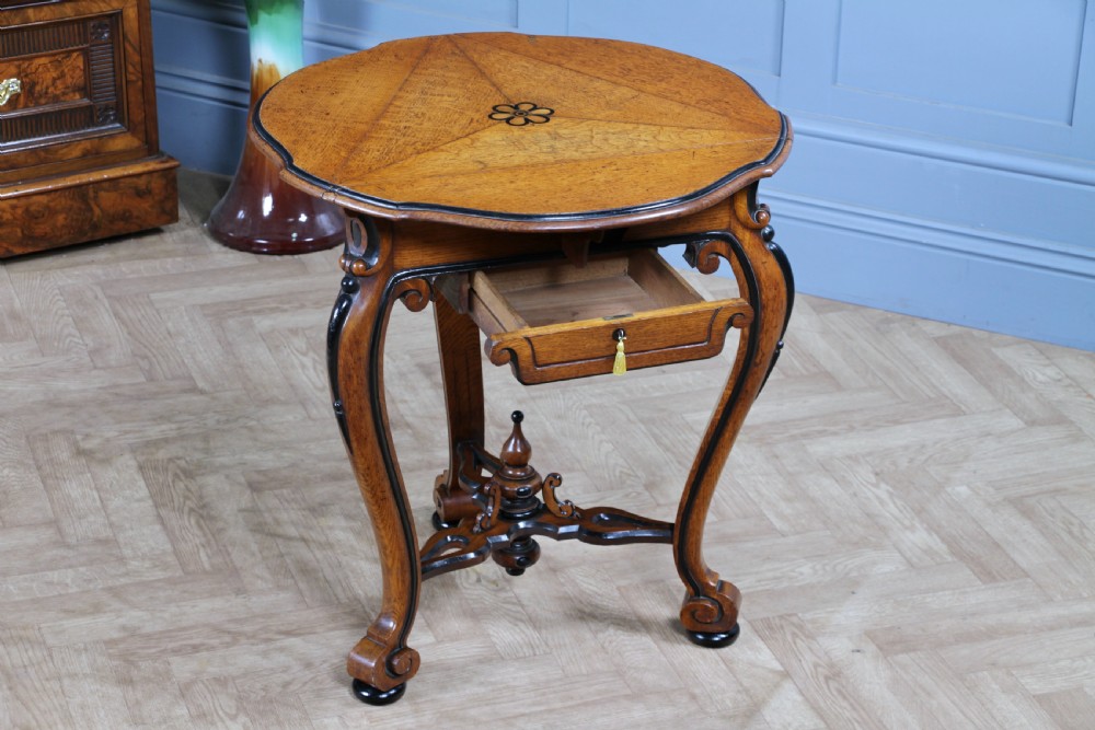 A Victorian Aesthetic Movement oak handkerchief table featuring ebonised accents, curved legs, and a triangular drop-leaf top with a central inlaid floral motif. View III