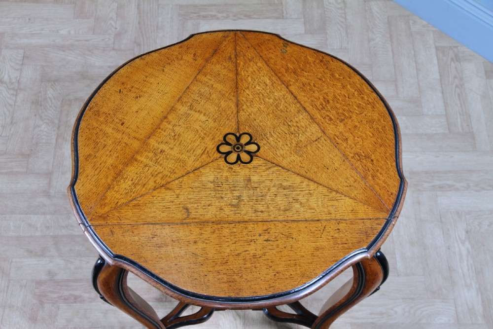 A Victorian Aesthetic Movement oak handkerchief table featuring ebonised accents, curved legs, and a triangular drop-leaf top with a central inlaid floral motif. View IV