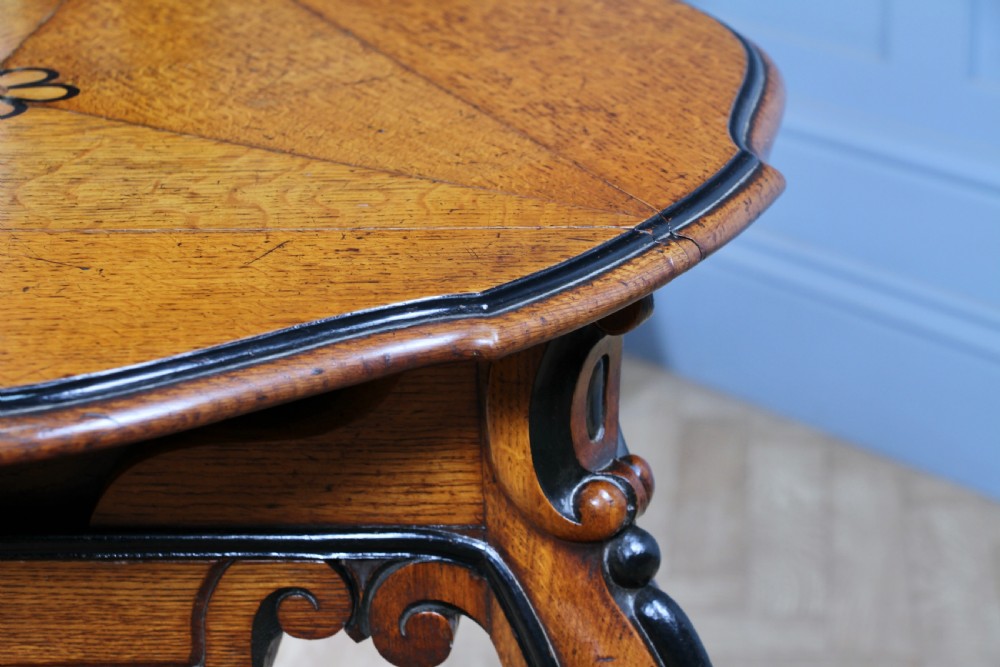 A Victorian Aesthetic Movement oak handkerchief table featuring ebonised accents, curved legs, and a triangular drop-leaf top with a central inlaid floral motif. View VII